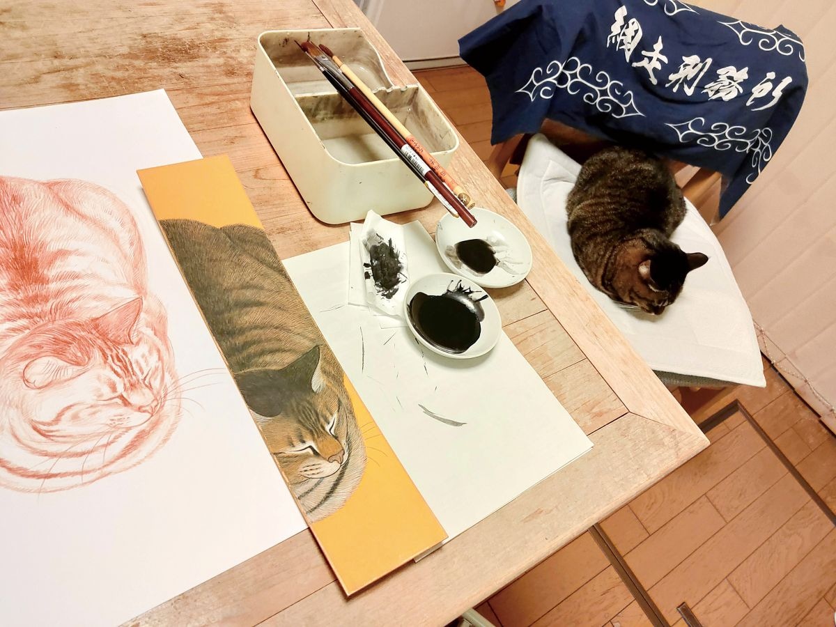 短冊作品「まるいこ」（360×75ｍｍ）の制作中。コイモちゃんが寄り添います　※画像出典：『コイモ 小熊香奈子画集』（辰巳出版）