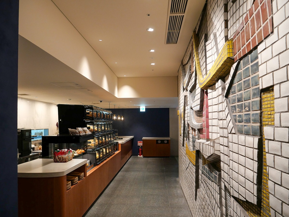 「OMOベーカリー」壁面には、旧市庁舎の泰山タイルレリーフ「海・波・船」を原位置保存（筆者撮影）