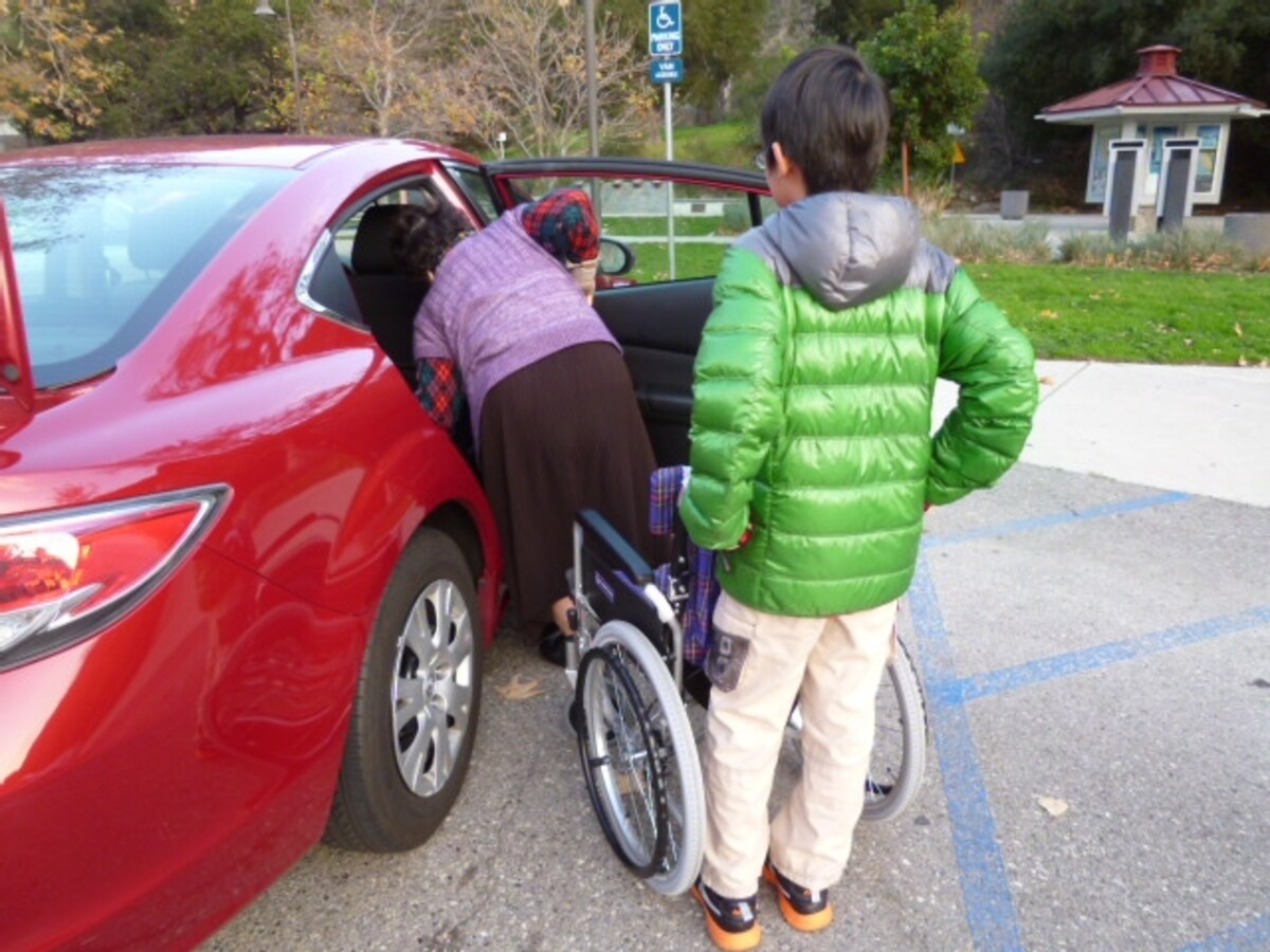 セダンの横に車椅子から降りた高齢者がセダンに乗り込もうとしている