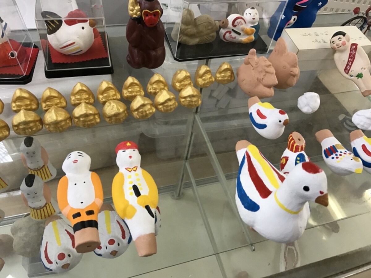 尾崎人形の工房にて。ガラスケースの上に乗った左端のオレンジ色の人物は近年復刻された「長太郎」。隣は「兵隊さん」。どこかとぼけていて、間の抜けた表情がいい。