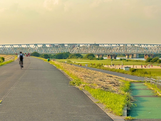 自転車で土手上を行く学生さんの背中から感じる青春の空気