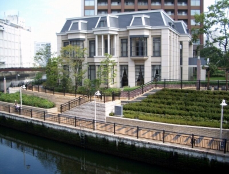 橋を渡ると左手に「エアタワー」（奥）の「ウェルカムハウス」が見える。この洋館風の内部は二層吹き抜け。自動扉を入るとカウンターデスクのフロントスタッフに出迎えられ、エスカレーターで2階へ。通路からタワーに向かう。