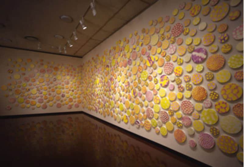 片山雅史さんの作品『皮膜2004－千の光』<BR>      向日葵の花芯部や水面の煌めきなどの自然界にある造型パターンを拡大し1000個の円形パネルに描いた作品。　表面は見る人の五感を引き出すよう様々な質感にになっている。