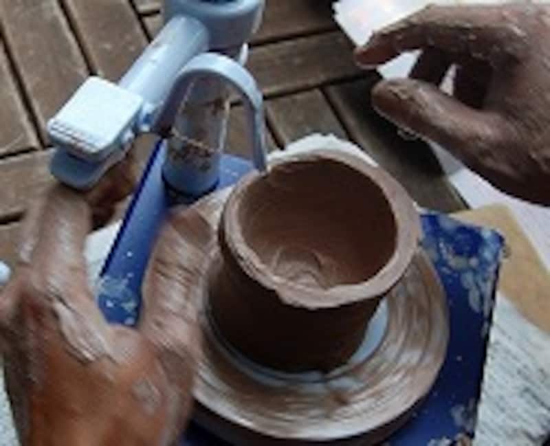 弓をつけたアームで、ろくろを回転させながら、口のでこぼこを切り落とす