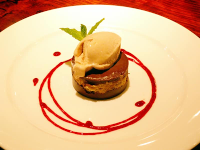 小さな円柱状のチョコレートケーキの上にアイスクリーム、周囲に細い輪を幾重にも描く紅いソース