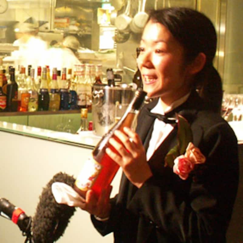 ソムリエのコスチュームで胸にピンクのバラを挿した笑顔の佐藤さん