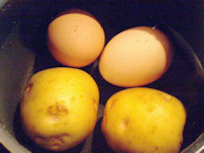 黒い鍋の中の水に赤玉の卵とジャガイモが2つずつ沈んでいる
