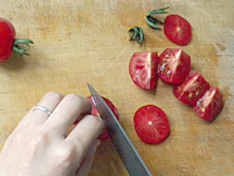 まな板の上でトマトのヘタを切り落として縦に4等分に切っています