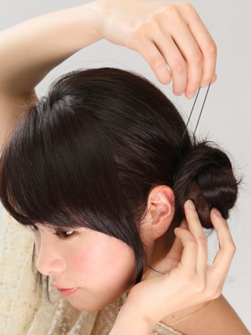 3三つ編みの根元を中心に巻きつけておだんごをつくり、Uピンで3～4ヶ所留めてしっかりと固定する。