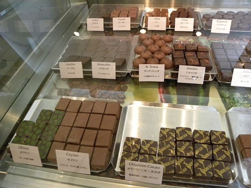 「オリジンーヌ・カカオ」のショーケースには、カカオ豆が散りばめられたディスプレイの上に、20種類程のボンボンショコラや、ショコラの様々なお菓子が並べられている