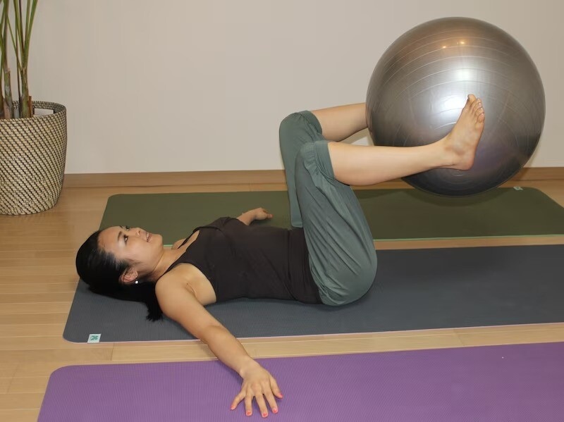 仰向けになり、両脚でボールを挟む