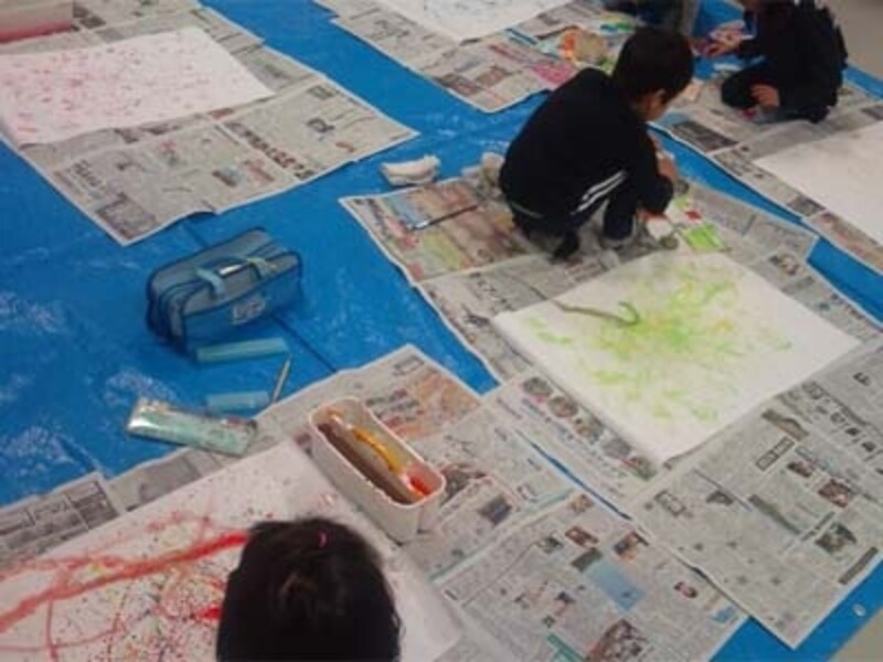 床に模造紙を敷いて制作する小学生