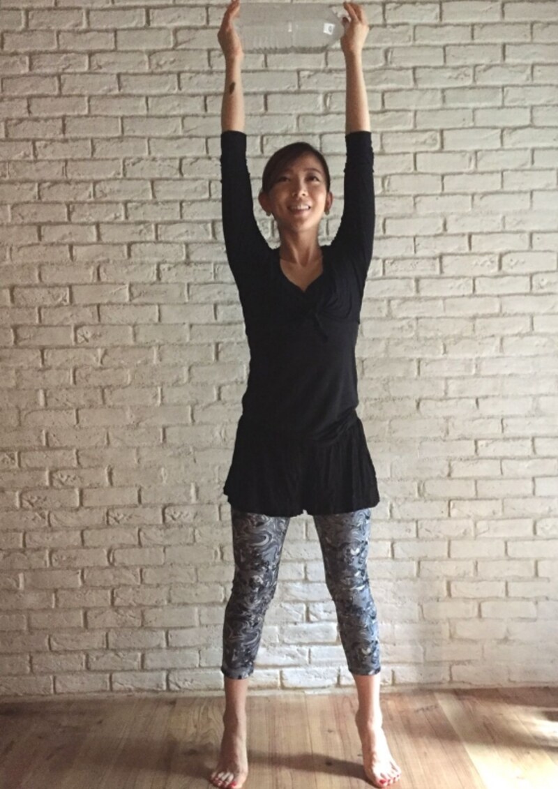 つまさき立ちでペットボトルを頭上に