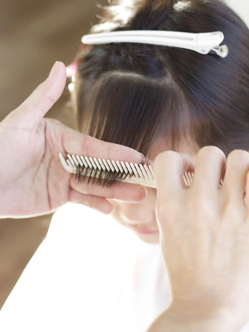 前髪にコームを入れながら手前に引き出す
