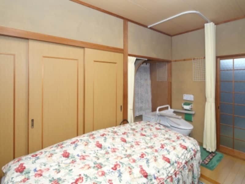 Sさんの寝室を掃き出し窓側から撮影した写真。奥の右手にあるのが茶の間への引き戸で、「ベッドサイド水洗トイレ」は左手に設置されています