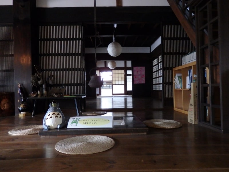 囲炉裏端で訪れた人を家の中へと招く小さな「トトロ」