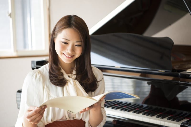 女性がピアノの前で楽譜を見ている写真