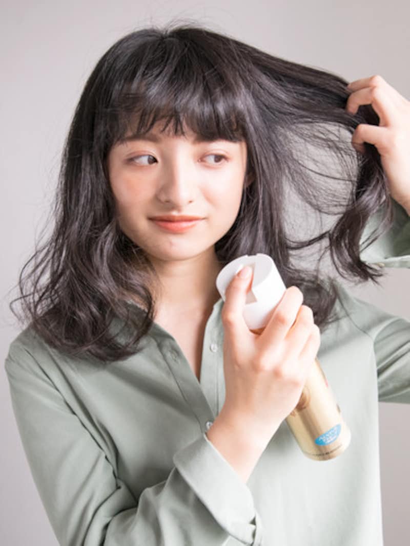 内側から空気を入れるように黒髪の巻き髪アレンジを固定する