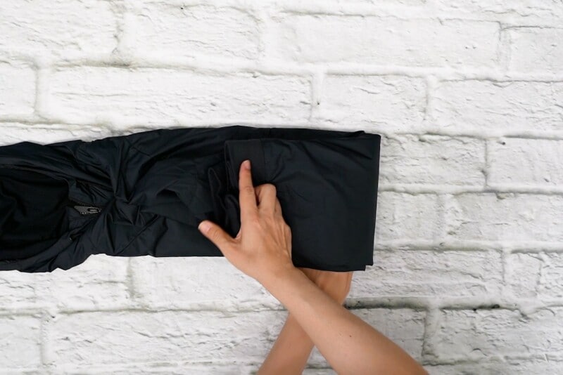 ファスナーを閉めてフードの幅になるように縦長に左右から折り、長細くなったものを折って（丸めて）、最後はフードにつっこみます。へ