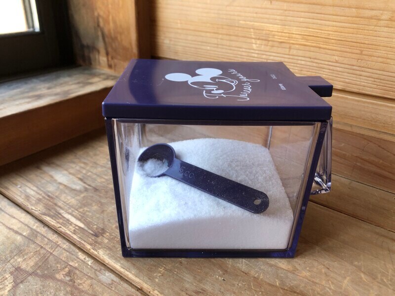 「ダイソーのSK キッチンポット、ワイド（ミッキー&ミニー）」に砂糖を入れている