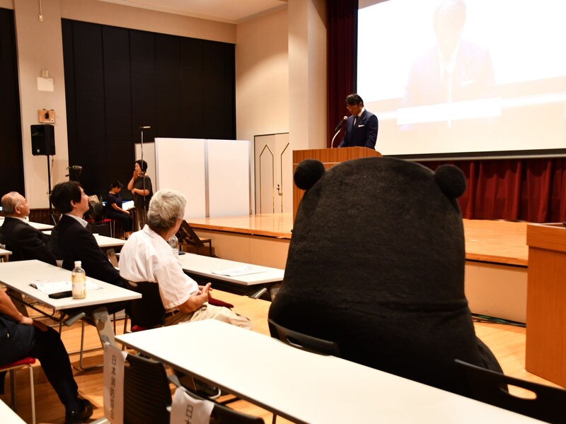 椅子に座ってスピーチに耳をかたむける=9月18日、横浜市