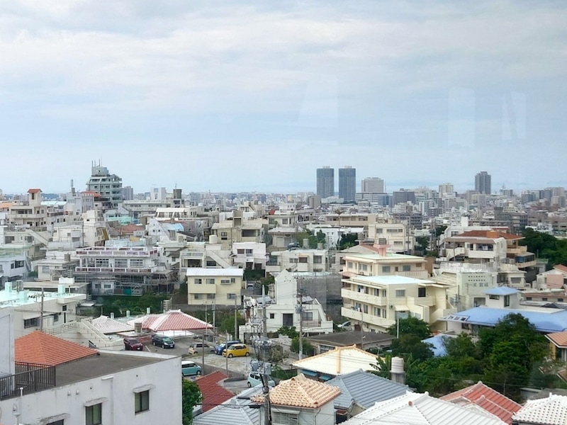 那覇の住宅街らしい風景。コンクリートの建物がぎゅうぎゅうにひしめき合う先に青い海が見える