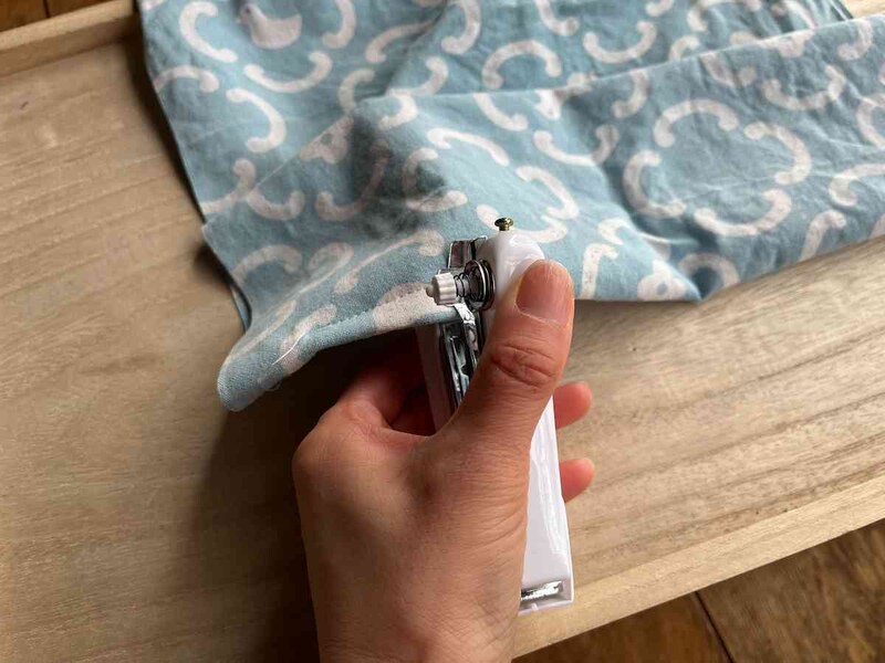 キャンドゥの「コンパクトハンディミシン」の布押さえを持ち上げて布をはさみ、カチカチと縫っていく