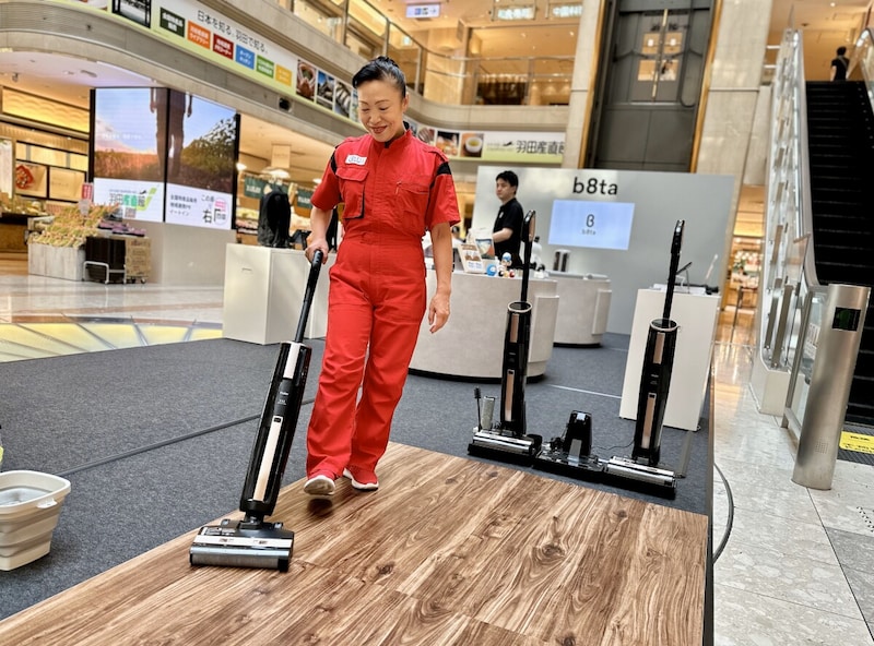 羽田空港で開催された体験イベントで、新津さんとハイアールが共同開発した「吸引式床拭き掃除機MIZUKI」(ハイアールご担当からいただいたURLにリンクしてあります) を説明する様子。ハンドル部分を持ち運びの楽なデザインにし、ヘッドの水量は、石や畳などのほか、日本のフローリング事情に合う特別なしくみを導入するなど独自の視点を盛り込んだ。中国の工場まで行って全製造ラインを細部までチェックしたそう。