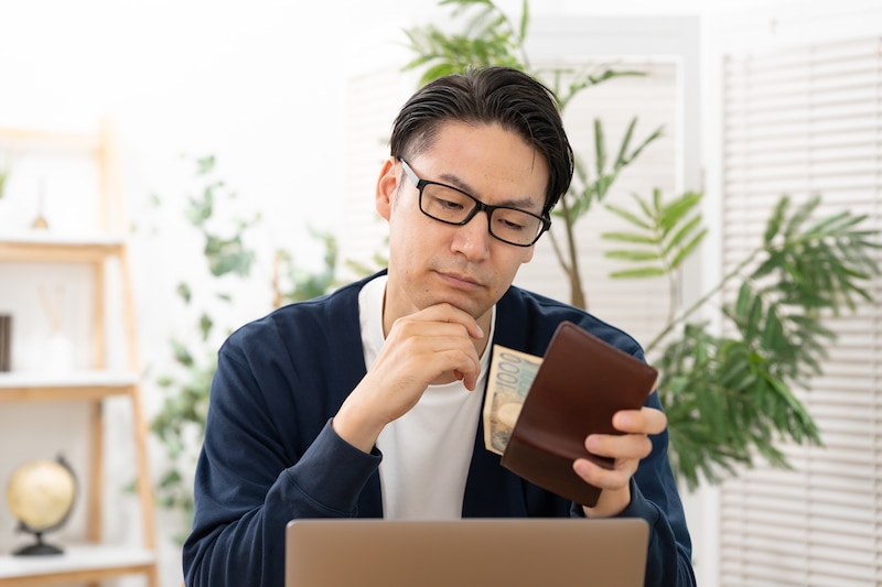 パソコンの前で財布を見つめる男性