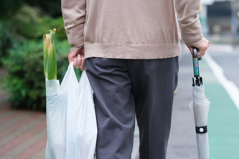 買い物袋を持ったシニア男性の後ろ姿