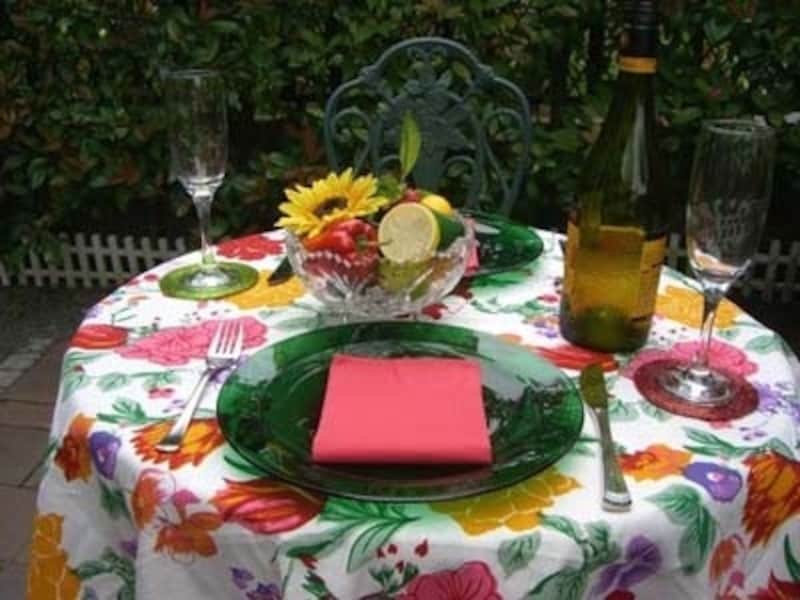 様々な花々が原色で描かれた南国風のテーブルクロスを敷いたコーディネートです。洋食器のグリーンのガラスのテーブルウェアとのコンビネーションも意外に合います