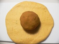 薄く打ち粉を振った板の上に取り出し、手の平で優しく押してガス抜きし、麺棒で伸ばして中央にかぼちゃ餡をのせる。