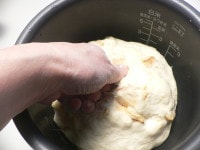 手をグーにして粉をつけて生地を押しつけて、ガス抜きをし、形を丸く整えて、上下を逆にして置き、ラップをかぶせて二次発酵させる。