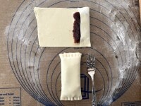 餅と粒あんをやや中央にずらし、巻き終わりが中心に来るようにパイ生地を包みます。両端が開かないように、上からフォークでパイ生地を押さえて閉じます。