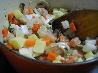 鍋にオリーブオイルとニンニク、たまねぎを入れて火にかけます。弱めの中火で炒め、たまねぎが透き通ってきたらエビ、にんじん、じゃがいも、白菜の茎を加えてよく炒めます。