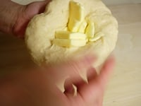 次にバターを加えます。手の上で生地を広げ、中央にバターを包み込むように練り込み、全体に馴染ませます。そして再びこね台の上で捏ねます。