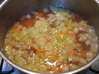 鍋にオリーブオイルとニンニクを入れて火にかけます。ニンニクの香りが立ってきたら、ハム、たまねぎ、にんじんを加え、たまねぎが透き通るまで炒めます。白ワインを加え、沸騰したら水とコンソメを加えます。アクをとりながら約7～8分煮ます。<br />