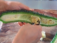 ゴーヤーを縦半分に切り、スプーンで白いワタと種を取り除き、1～2mm幅の薄切りにします。<br />