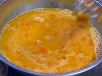鍋の温かいみかん果汁をおたまで掬い、混ぜながらボールに少しずつ流し入れてゆく。このとき卵液を泡立てないように注意する。 <br />