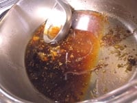肉を取り出した煮汁の表面にある余分な脂（冷めると白くなる）は、お玉を使ってすくい取ります。