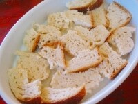 パンを適当にちぎり、薄くオリーブオイルを塗った耐熱皿に入れ、牛乳を注いでパンをふやかします。 <br />