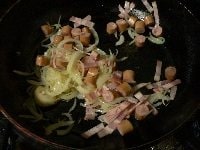 細切りベーコンと小口切りウインナーを1分炒める。沸騰した湯に塩を入れ、パスタを茹ではじめる。