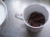 チョコレートを小さく割ってカップに入れる。小鍋か電子レンジで牛乳を温める。 <br />