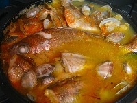 魚介は、うろこやはらわたを取るなど、適宜下ごしらえをします。オーブンに入れられる鍋にアサリ以外の魚介を並べ、表面にオリーブオイルを塗ります。そこにスープをたっぷり注ぎます。サフランを軽く乾燥させ、もみほぐしてからスープに加えます。<br />
<br />
200度のオーブンに入れ、魚にぎりぎり火が通るぐらいまでローストします。<br />
魚に火が通る少し前にアサリを加え、アサリが開いたらオーブンから出します。<br />