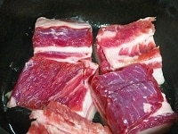 豚バラ肉を5cm角程度に切って、油を入れた鍋に入れ、表面が色づくまで弱火で炒めます。<br />