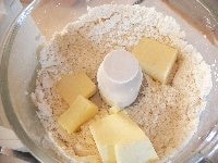（生地作り）フードプロセッサーに小麦粉、塩、砂糖を入れて10秒ほど攪拌（かくはん）する。次に冷えたバターを加えて攪拌し、さらさら状態にする。 <br />