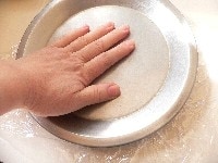 温かいご飯に片栗粉を加えて混ぜ合わせ、二等分してまん丸に、きつく握り、 ラップを広げた上にのせ、もう一枚のラップをかぶせ、平らな皿を重ねてギュッと押しつぶす。