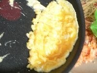 卵1コと、とんかつを作った時の残りの卵を（合計1コ半位）を軽くかき混ぜて、塩コショウする。フライパンにサラダ油を熱し、卵液を流しいれ、大きく混ぜながら焼いて、半熟状態になったら、チキンライスの上にのせる。