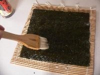 巻きすの上に板海苔を置き、ハケでごま油を薄く塗り、塩を少しずつまんべんなくふりかける。