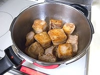 圧力鍋にバター5gとサラダ油小さじ1を入れ、中火にかけます。バターが溶けたら豚肉を入れ、全面焼き色をつけます。焼き色がついたらキッチンペーパーにのせて余分な油を切ります。<br />